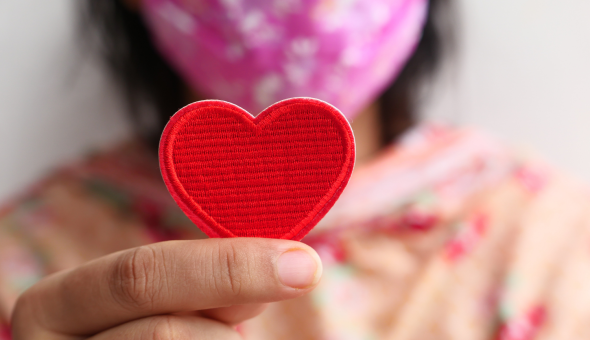 a masked student holds a small red paper heart near the camera