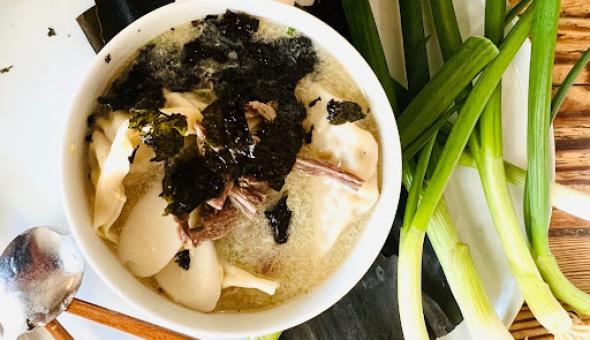 A bowl of rice cake soup (tteokguk) garnished with roasted seaweed on a platter with green onions eggs, chopsticks, and spoon