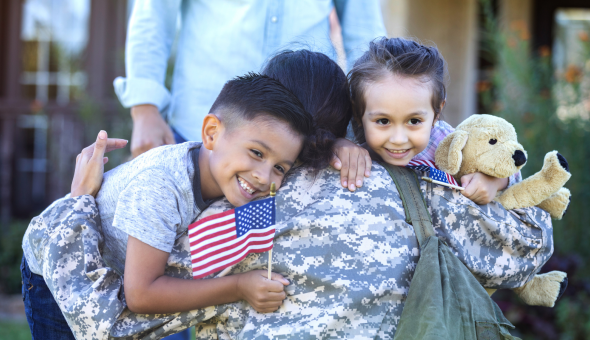Two young children welcome and and hug their mother who is returning from active duty. She is wearing a uniform.