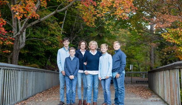 Kathy Higgins and her partner Sherry and their four children stand together on a bridge under orange and green autumn leaves.
