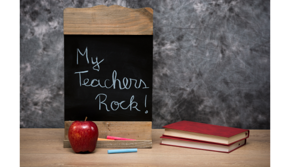 Small chalkboard that reads "My teachers rock!" sits next to a red apple and books.