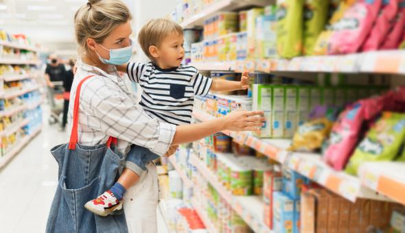 Woman and small child browsing the shelves of a grocery store. The woman is wearing a face mask.