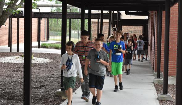 students walking in an outdoor hallway while listening to The Walking Classroom