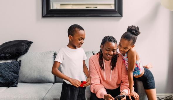 Two kids look over the sholder of an adult who is holding a phone; all three are smiling