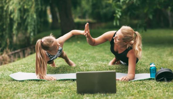 Mother and daughter giving high fives while doing yoga in the grass with a laptop in front of them