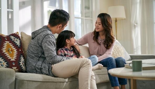 Two parents and young child sit on a sofa talking together.